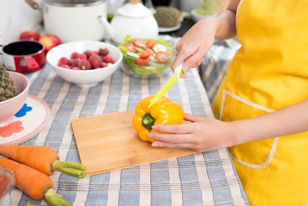 Linda mulher asiática cortando pimenta na cozinha