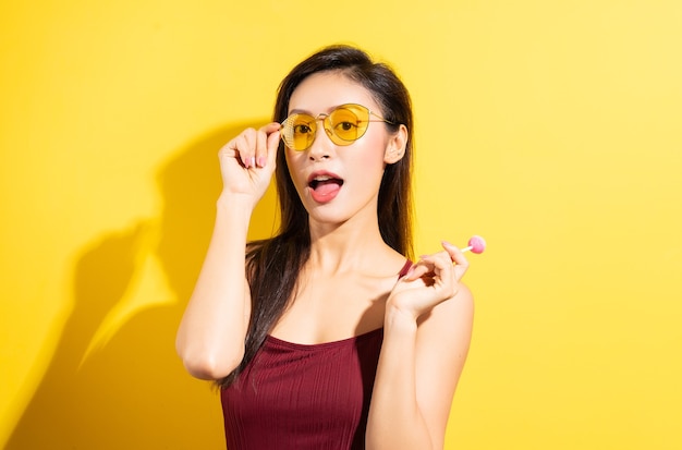 Linda mulher asiática em maiô vermelho e comendo pirulitos em uma parede amarela