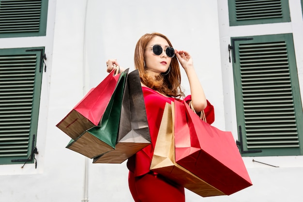 Linda mulher asiática em óculos de sol, carregando sacolas de compras