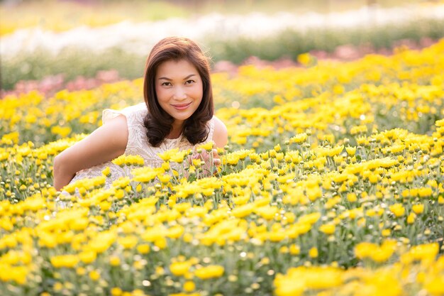 Linda mulher asiática em pé e sorrindo no jardim de flores tropicais com maneira de felicidade com a luz solar quente de fundo.