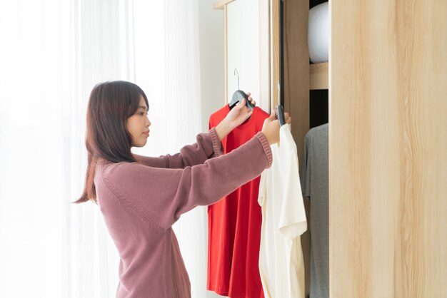 Linda mulher asiática escolhendo roupas em um quarto