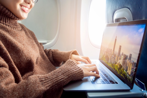 Linda mulher asiática está trabalhando com o laptop no avião