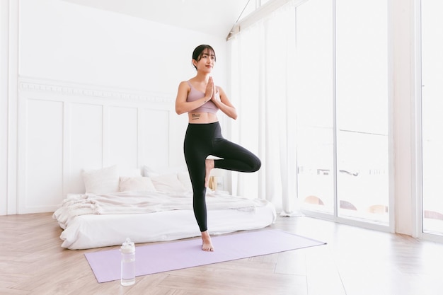 Linda mulher asiática feliz em pé na postura de Vrksasana fazendo exercícios de ioga.