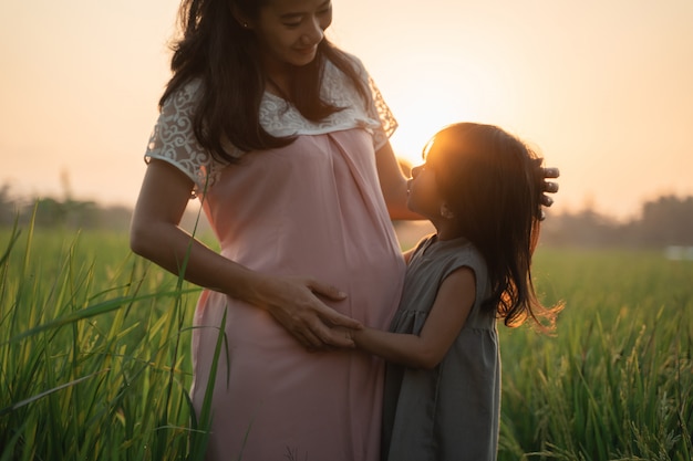 Linda mulher asiática grávida com filha brincando na barriga