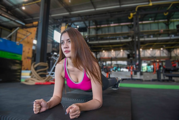 Linda mulher asiática joga fitness na academiaA menina da Tailândia tem um corpo esbeltoTempo para o exercícioAs pessoas adoram a saúdeEsticar o corpo antes do treinoMulher esportiva aquecer bodyplanking no chão
