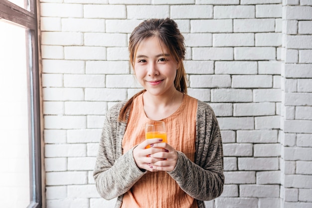 Linda mulher asiática relaxante na casa aconchegante com suco de laranja