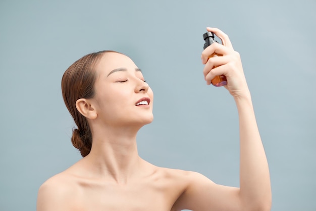 Linda mulher asiática segurando a garrafa de água spray isolada de fundo branco