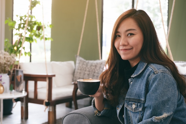 linda mulher asiática segurando e tomando café quente no café