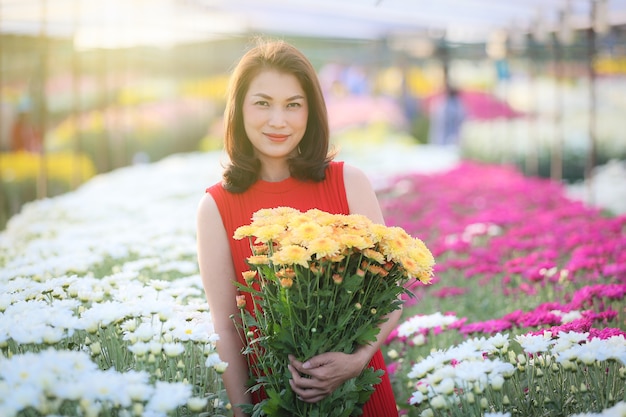 Linda mulher asiática segurando flores amarelas nas mãos com maneira de orgulho, proprietário do jardim de flores satisfeito com flores de boa qualidade para venda.