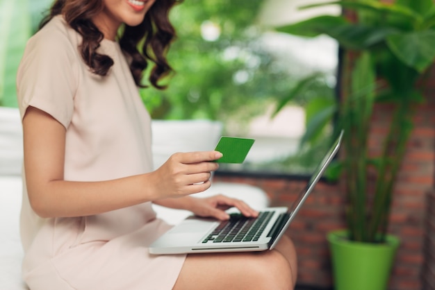 Linda mulher asiática segurando um cartão de crédito e fazendo compras online