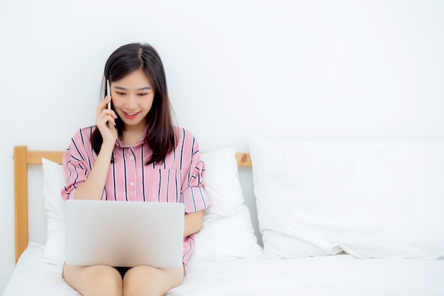 Linda mulher asiática sentada na cama usando o computador portátil