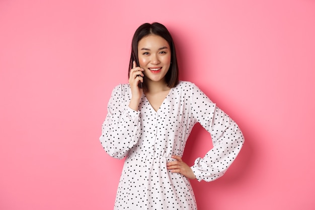 Linda mulher asiática, tendo uma conversa móvel, fazendo ligação e sorrindo, em pé rosa.