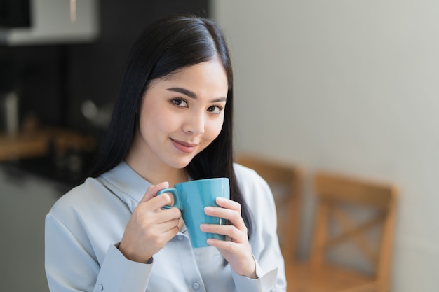 Linda mulher asiática tomando café e trabalhando em casa pela manhã