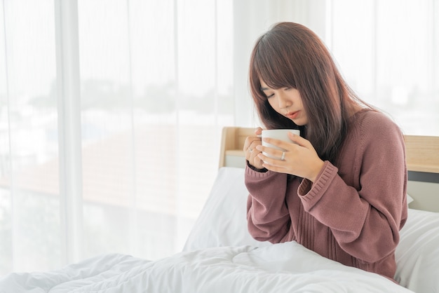 Linda mulher asiática tomando café na cama pela manhã