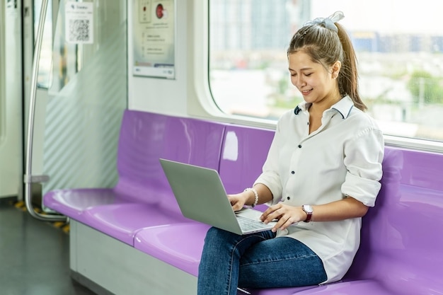 Linda mulher asiática trabalhando com urgência em um laptop no trem elétrico pela manhã