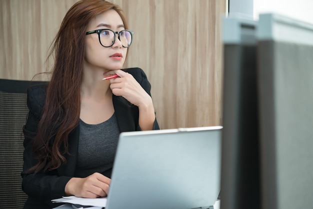 Linda mulher asiática trabalhando no escritório à noiteTrabalhador tailandês trabalha horas extras para a empresaUma empresária pensa