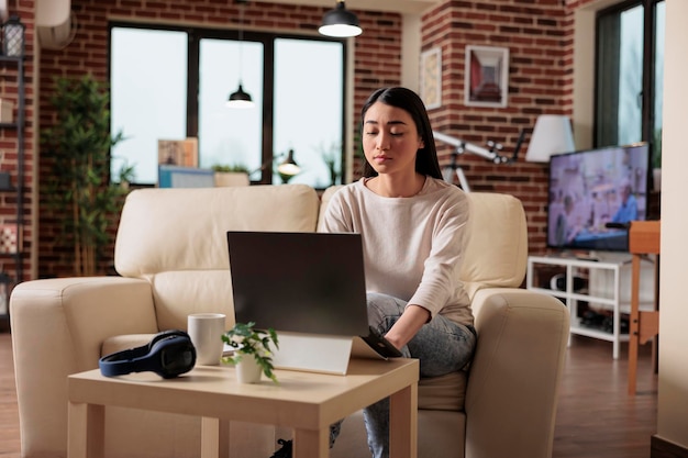 Linda mulher asiática trabalhando no laptop em sua casa. Estilo de vida de tecnologia de internet de usuário de computador de negócios trabalha em casa, freelancer feliz na sala de estar