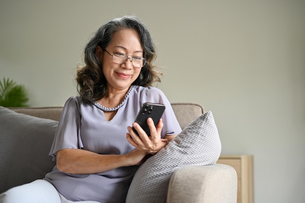 Linda mulher asiática usando óculos usando seu smartphone para ler uma notícia online