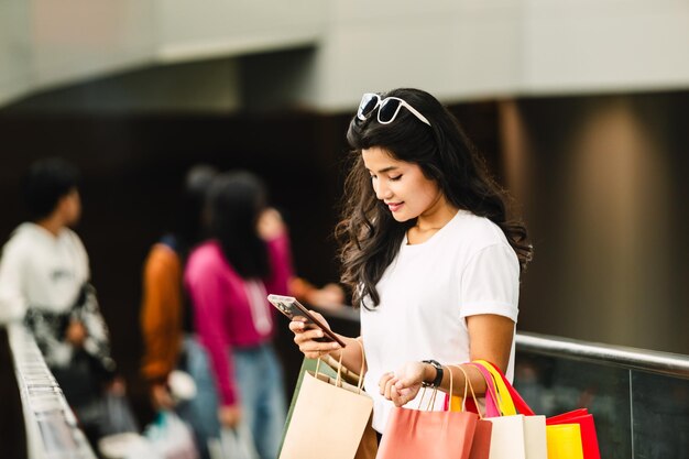 Linda mulher asiática usando telefone inteligente com sacola de compras na cidade