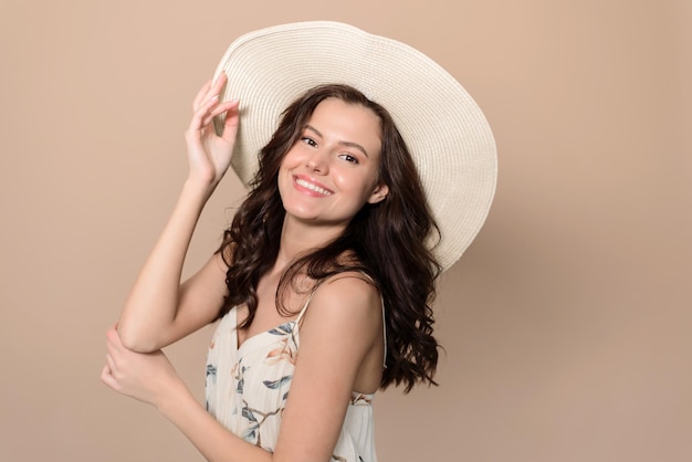 Linda mulher atraente em um vestido de verão e um chapéu de palha posando em uma tendência de estilo de moda de verão de fundo bege