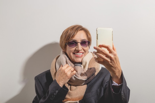 Linda mulher baby boomer de meia idade em óculos de sol tira selfie no smartphone à luz do sol