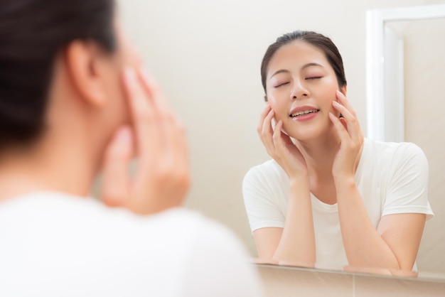 linda mulher bonita no banheiro da sala de estar na frente do espelho mantém a pele facial saudável no despertar da manhã todos os dias.