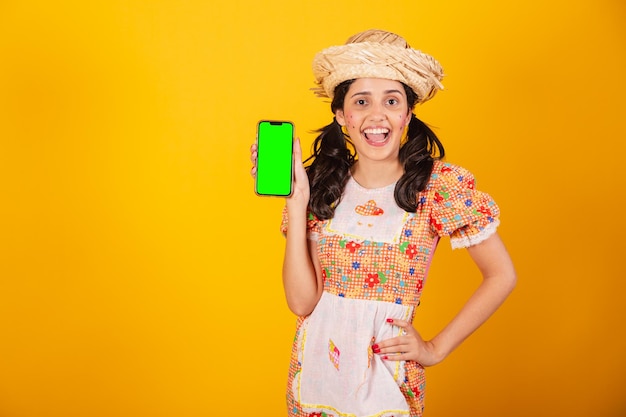 Linda mulher brasileira com roupas de festa junina segurando smartphone com tela verde