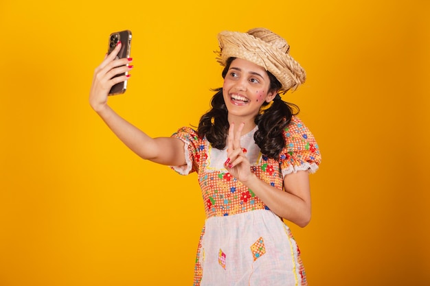 Linda mulher brasileira com roupas de festa junina tirando autorretrato com smartphone