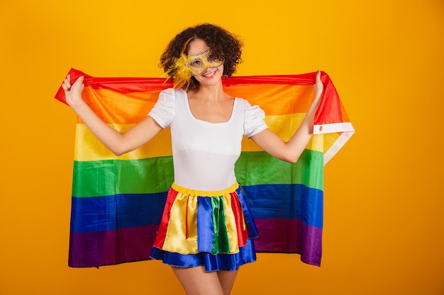 Linda mulher brasileira vestida com roupas de carnaval saia colorida e camisa branca usando rímel segurando a bandeira lgbt