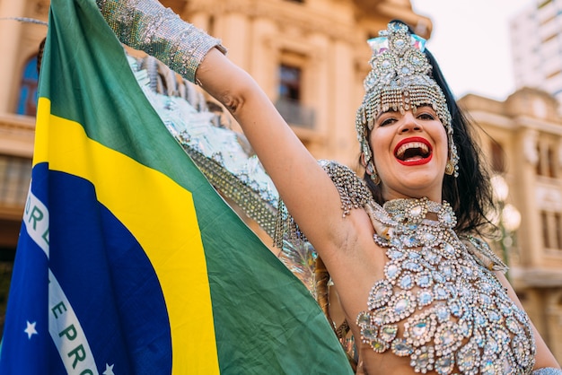 Linda mulher brasileira vestindo fantasia colorida de carnaval e a bandeira do Brasil durante o desfile de carnaval na cidade.