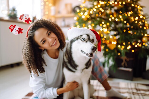 Linda mulher brincando e se divertindo com seu cachorro enquanto está sentado perto da árvore de natal