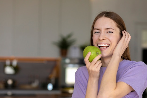 Linda mulher caucasiana com dentes brancos sorrindo e comendo uma maçã verde, estilo de vida saudável