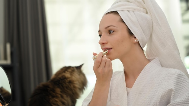 Linda mulher caucasiana com maquiagem natural aplicando protetor labial na frente do espelho Conceito de beleza e cosméticos