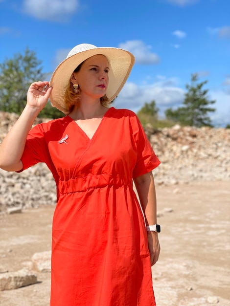 Linda mulher caucasiana de vestido vermelho usando chapéu de palha sorrindo na praia