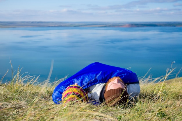 Linda mulher caucasiana e bonito homem escocês deitado embrulhado em um saco de dormir e se abraçando ao fundo do acampamento, paisagem do lago e colinas. casal apaixonado, caminhantes viajando