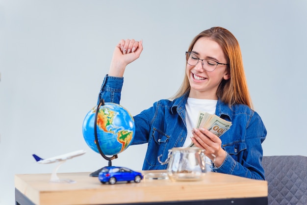 Linda mulher caucasiana em camisa jeans conta dinheiro para futura viagem ao redor do mundo e sente a felicidade.