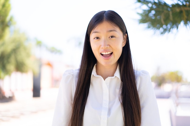 Linda mulher chinesa ao ar livre com expressão facial de surpresa