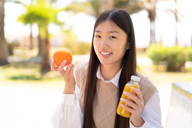 Linda mulher chinesa ao ar livre segurando uma laranja e um suco de laranja