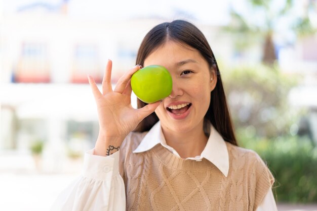 Linda mulher chinesa ao ar livre segurando uma maçã com expressão de surpresa