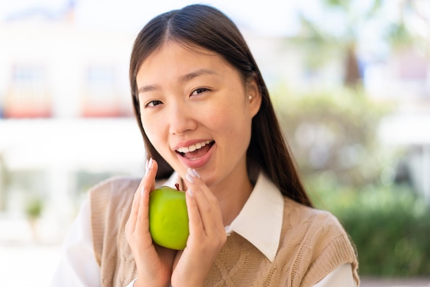 Linda mulher chinesa ao ar livre segurando uma maçã com expressão de surpresa