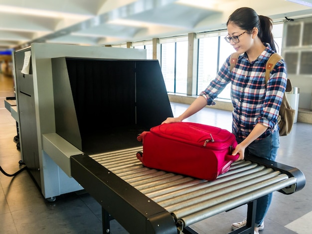 linda mulher chinesa colocar bagagem no ponto de verificação do scanner. Faixa de máquina de raio-x de bagagem na correia transportadora no aeroporto. foco seletivo