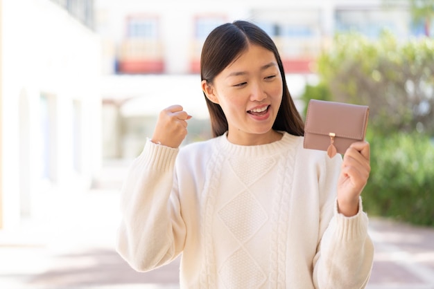 Linda mulher chinesa segurando uma carteira ao ar livre comemorando uma vitória