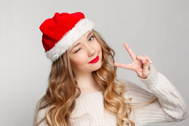 Linda mulher com chapéu de Papai Noel, piscando e sorrindo.