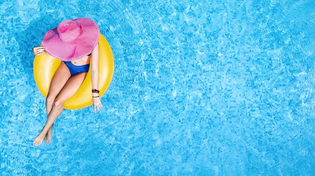 Linda mulher com chapéu na piscina, vista aérea de cima, jovem de biquíni relaxa e nada no anel inflável donut e se diverte na água, resort tropical de férias