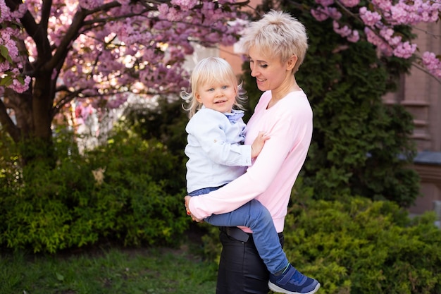 Linda mulher com garotinho perto de árvore florescendo de sakura rosa Conceito de primavera