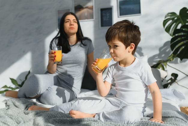 Linda mulher com o filho bebendo suco pela manhã na cama