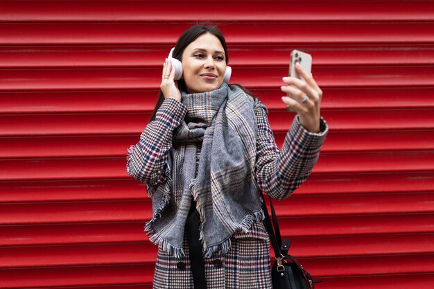 Linda mulher com roupas de outono faz uma selfie em fones de ouvido no fundo de um relevo vermelho