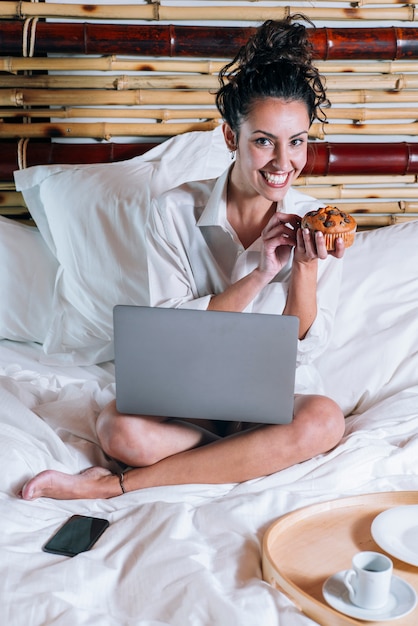 Linda mulher com telefone e laptop na cama