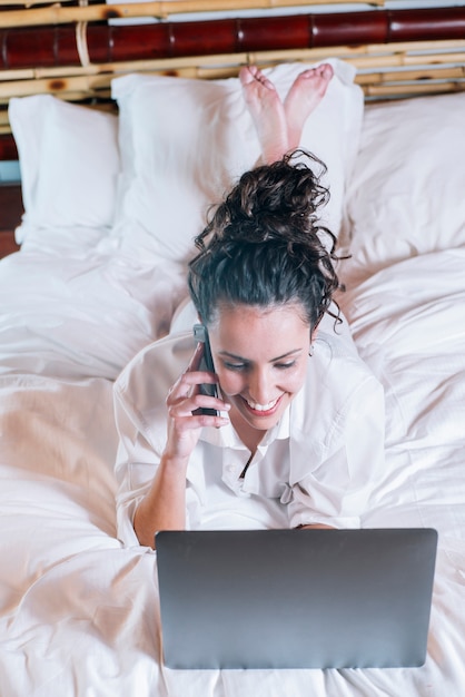 Linda mulher com telefone e laptop na cama