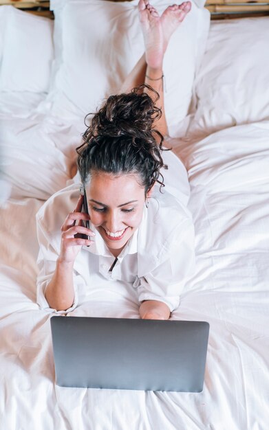 Linda mulher com telefone e laptop na cama